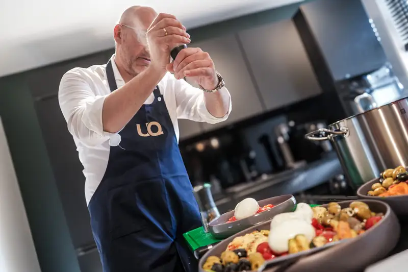 Koch mit UQ-Schürze würzt Antipasti im UnternehmerQuartier